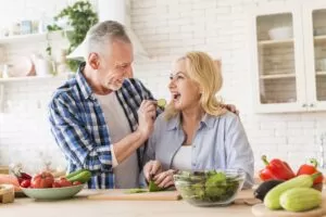 senior man feeding cucumber slice to her wife in the kitchen